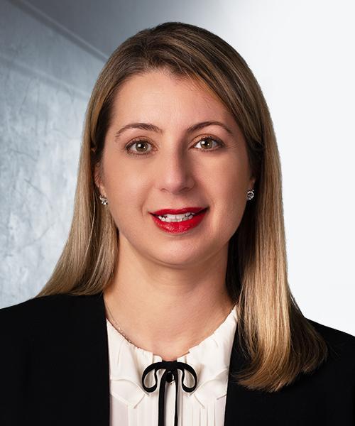 A photograph of Elizabeth Reynolds in a white shirt with a black blazer, against a gray background.
