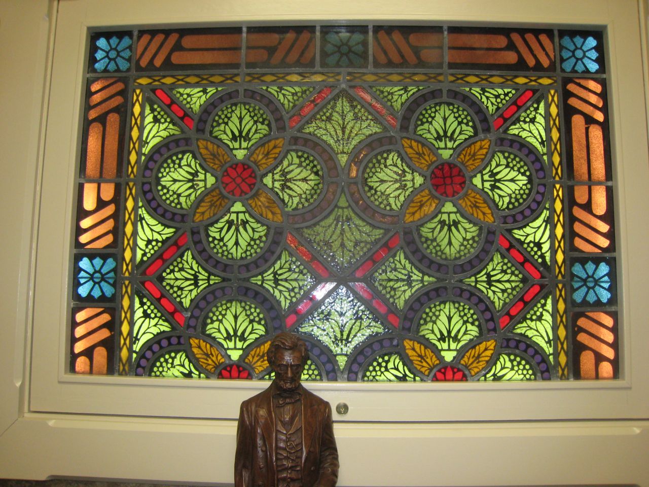 A statue of Abraham Lincoln stands in front of a stained glass window.