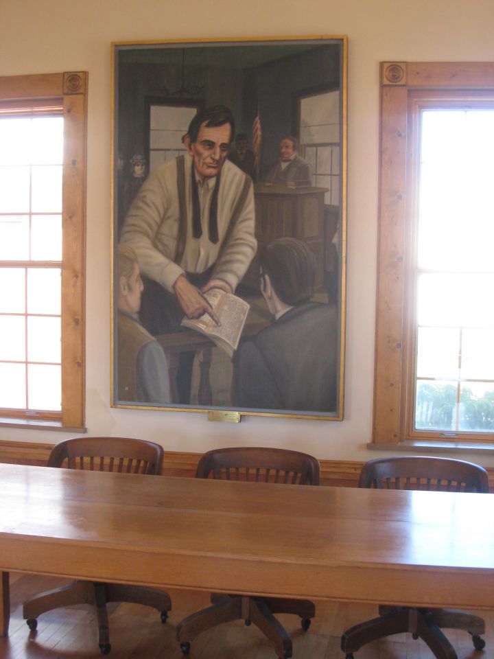 Jury table in Lincoln Courtroom with painting of Lincoln showing Farmers Almanac to jury in background.