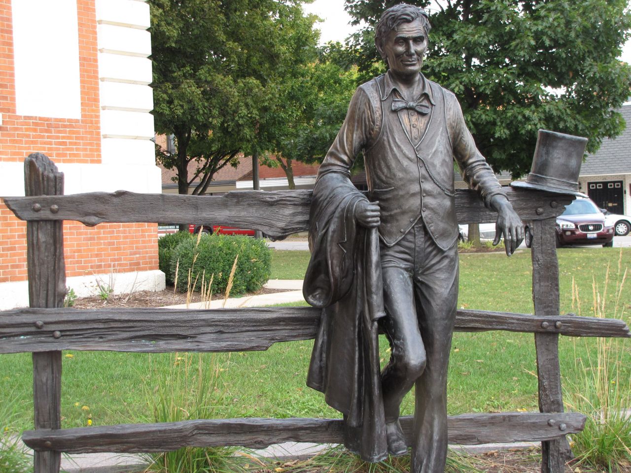 Abraham Lincoln stands next to a split rail fence just outside the courthouse entrance.
