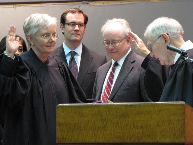 Mary Jane Theis (left) is sworn-in by retiring Chief Justice Thomas Fitzgerald as her son and husband look on.