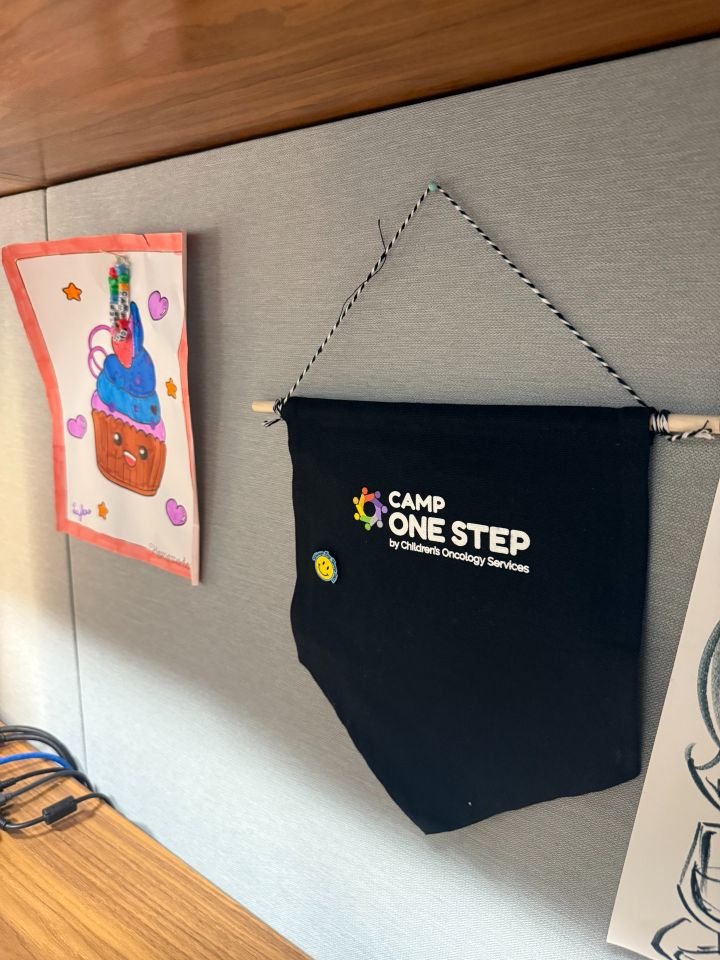 Madeline Domenichella: "My prized possession is a pennant from Camp One Step, an organization that provides camp experiences for children with cancer and their families. I got involved with Camp One Step when I ran the Chicago Marathon in 2024 for their charity team. I received this pennant for volunteering for this year's Chicago Day Camp where I assisted with field trips, activities, and arts and crafts (including the drawing seen on the left). I keep the pennant in my office to honor the inspiring kids and their families."