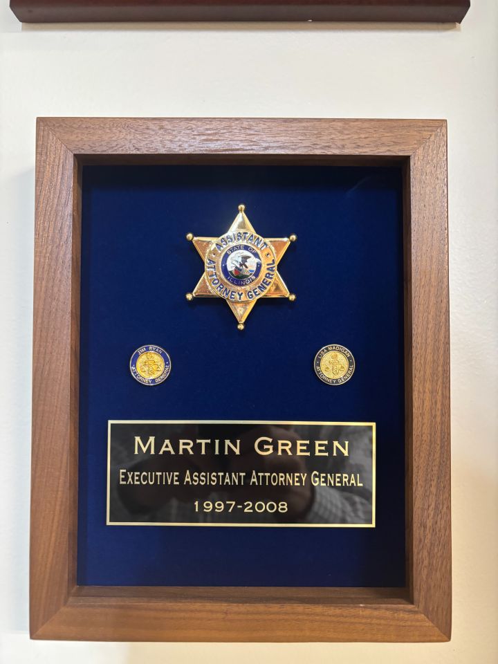 Martin Green: "The shadow box contains my badge from the Illinois Office of the Attorney General where I served as Executive Assistant Attorney General for Attorneys General Jim Ryan and Lisa Madigan. Underneath the badge are staff pins for Ryan and Madigan that include the scales of justice. Upon leaving the AOG for the private sector, I purchased the assigned numbered badge as a memento of my service. I am honored to have it hanging in my office as a reminder of the leadership and service of two exceptional Attorneys General who served our state in an exemplary manner."