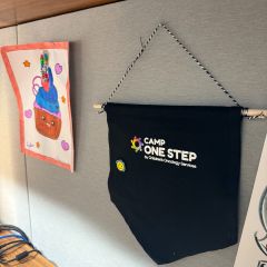 Madeline Domenichella: "My prized possession is a pennant from Camp One Step, an organization that provides camp experiences for children with cancer and their families. I got involved with Camp One Step when I ran the Chicago Marathon in 2024 for their charity team. I received this pennant for volunteering for this year's Chicago Day Camp where I assisted with field trips, activities, and arts and crafts (including the drawing seen on the left). I keep the pennant in my office to honor the inspiring kids and their families."